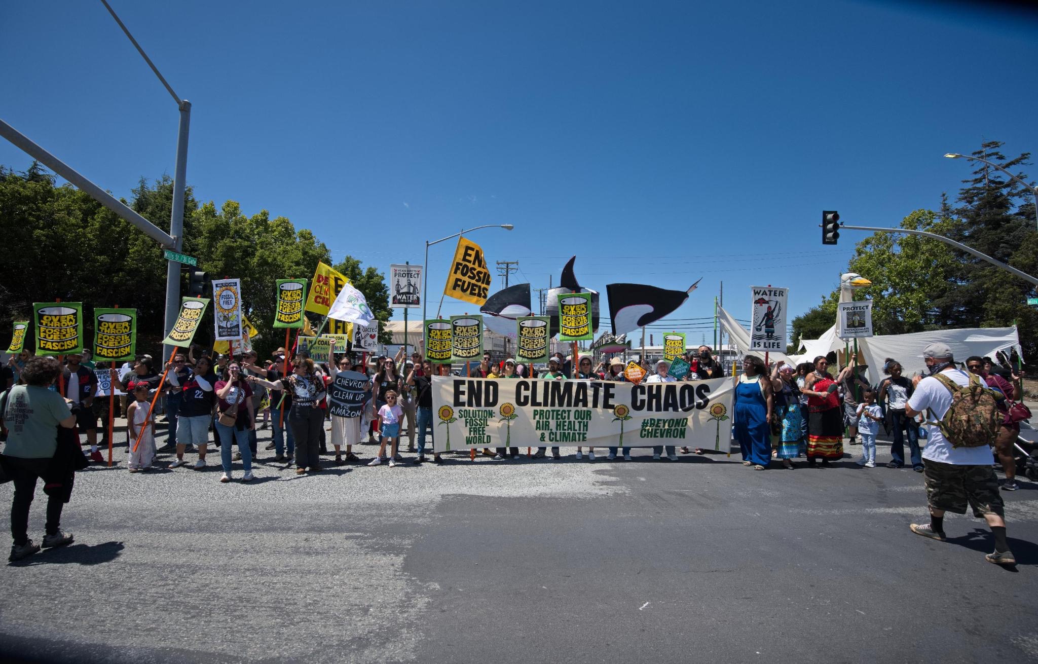A large, diverse crowd of Richmond residents of all ages marching with signs reading "End Climate Chaos," "Protect Our Air, Health & Climate," and "Beyond Chevron."