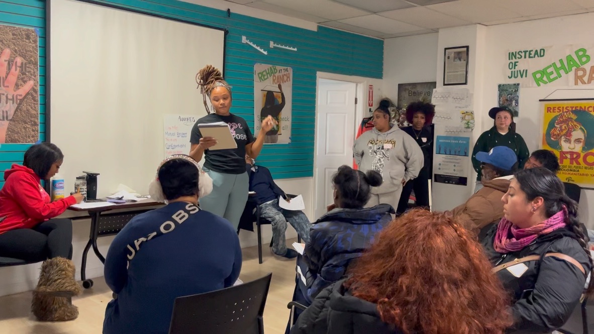 A community organizer presenting to a seated group in a workshop space.
